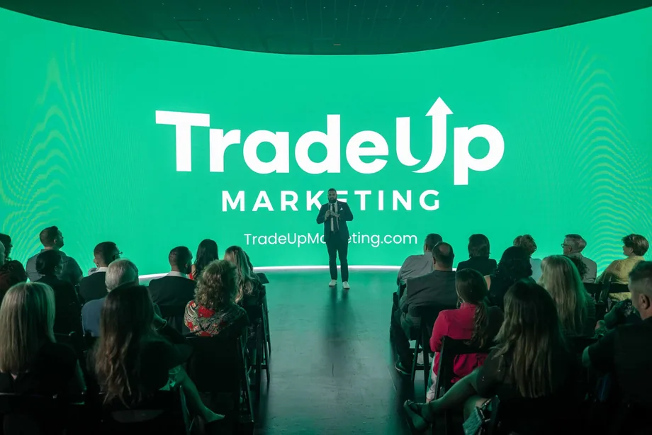 Jordan Lung presenting to a seated audience in front of a TradeUp Marketing branded stage screen