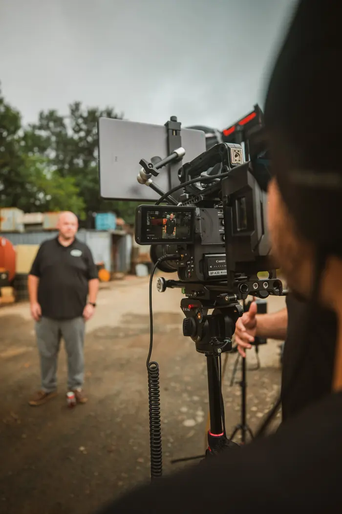 Camera operator framing a business owner on a job site, seen through the camera monitor