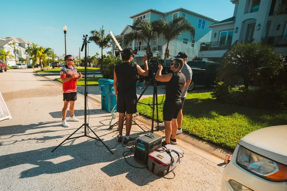 Crew filming a contractor on a sunny Florida residential street with lights and a boom