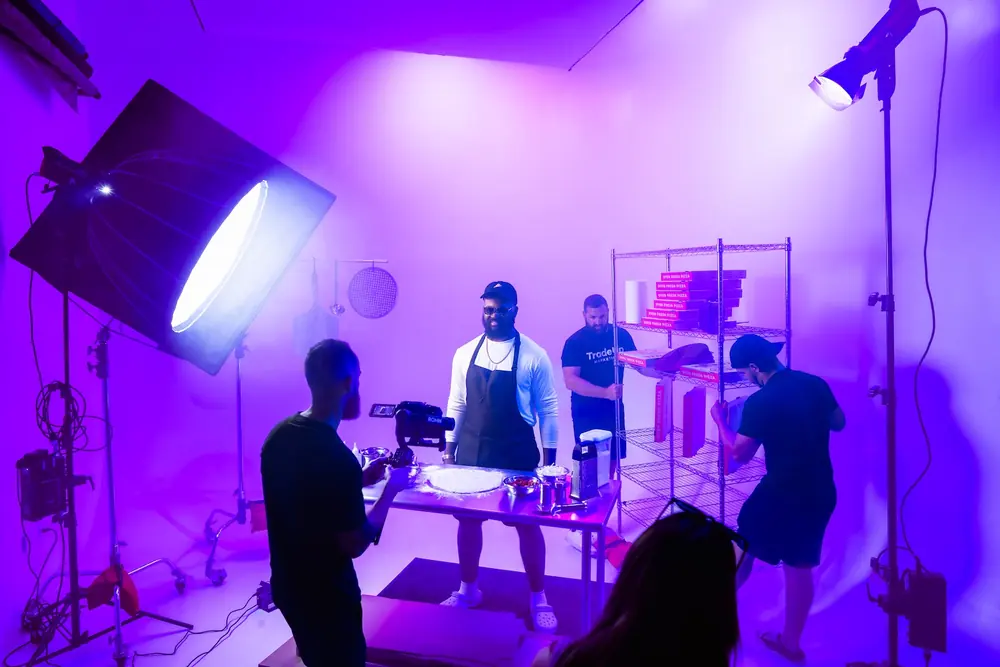 Studio product shoot bathed in purple light with a chef tossing pizza dough on camera