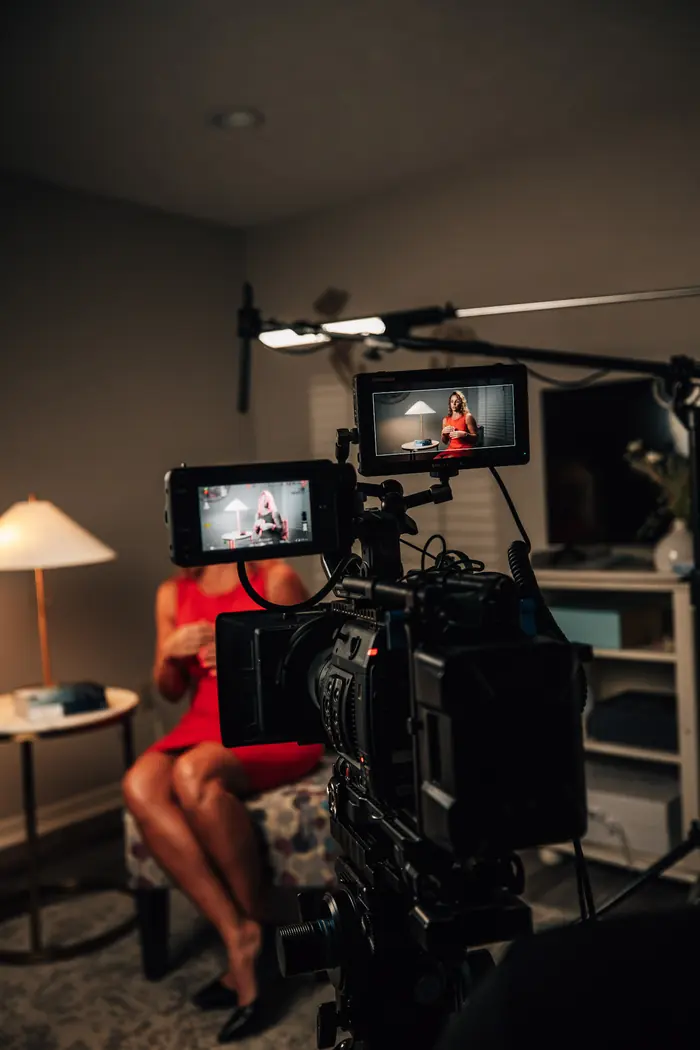 Two camera monitors framing a woman in a red dress during a seated testimonial interview