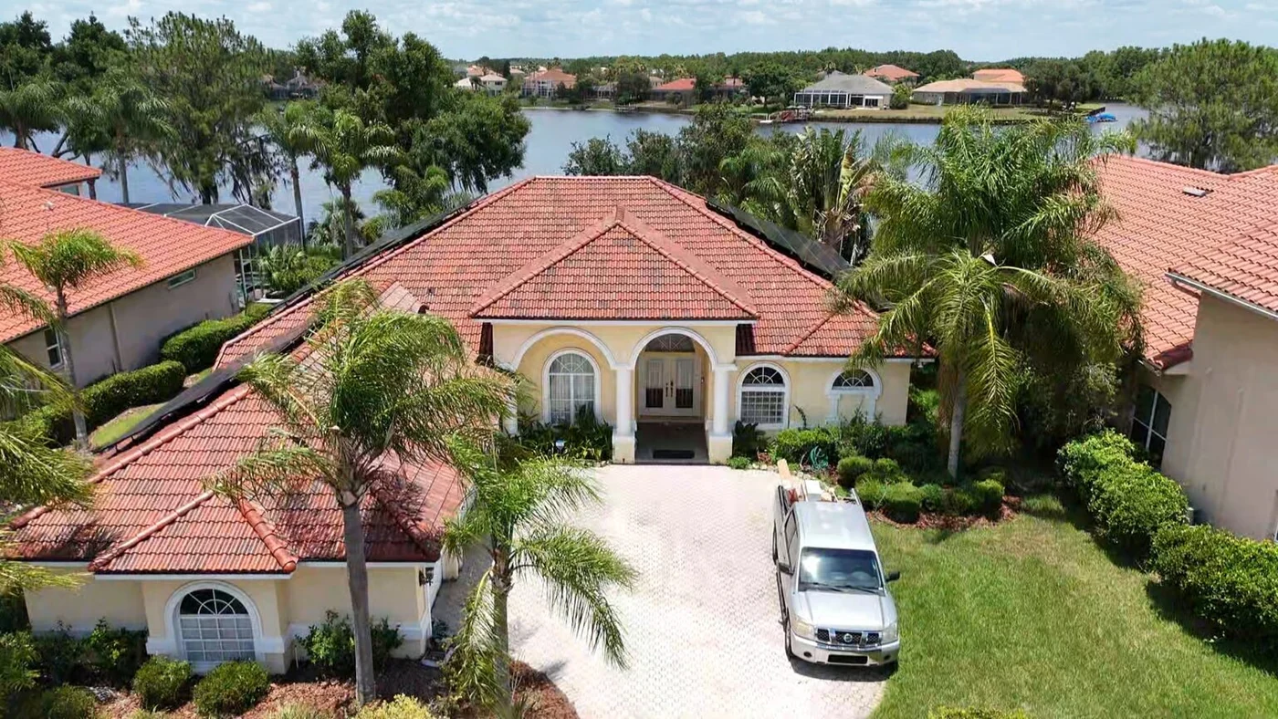 Greentek project photo — a drone view of a lakefront Florida home with a terracotta barrel tile roof, palms and a paver driveway