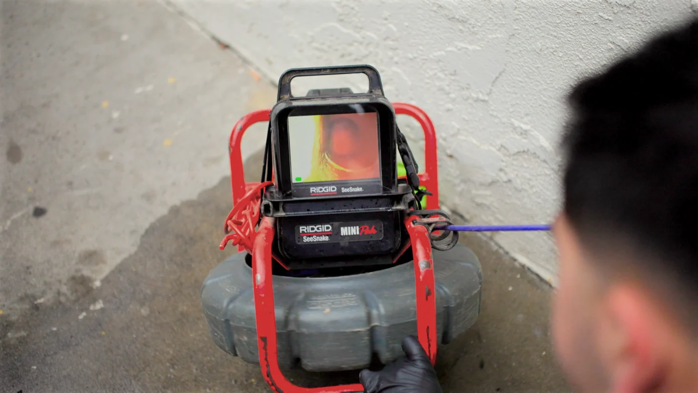 Ramco project photo — a technician feeding a push rod into a clean-out, looking down at the live picture on a RIDGID SeeSnake monitor
